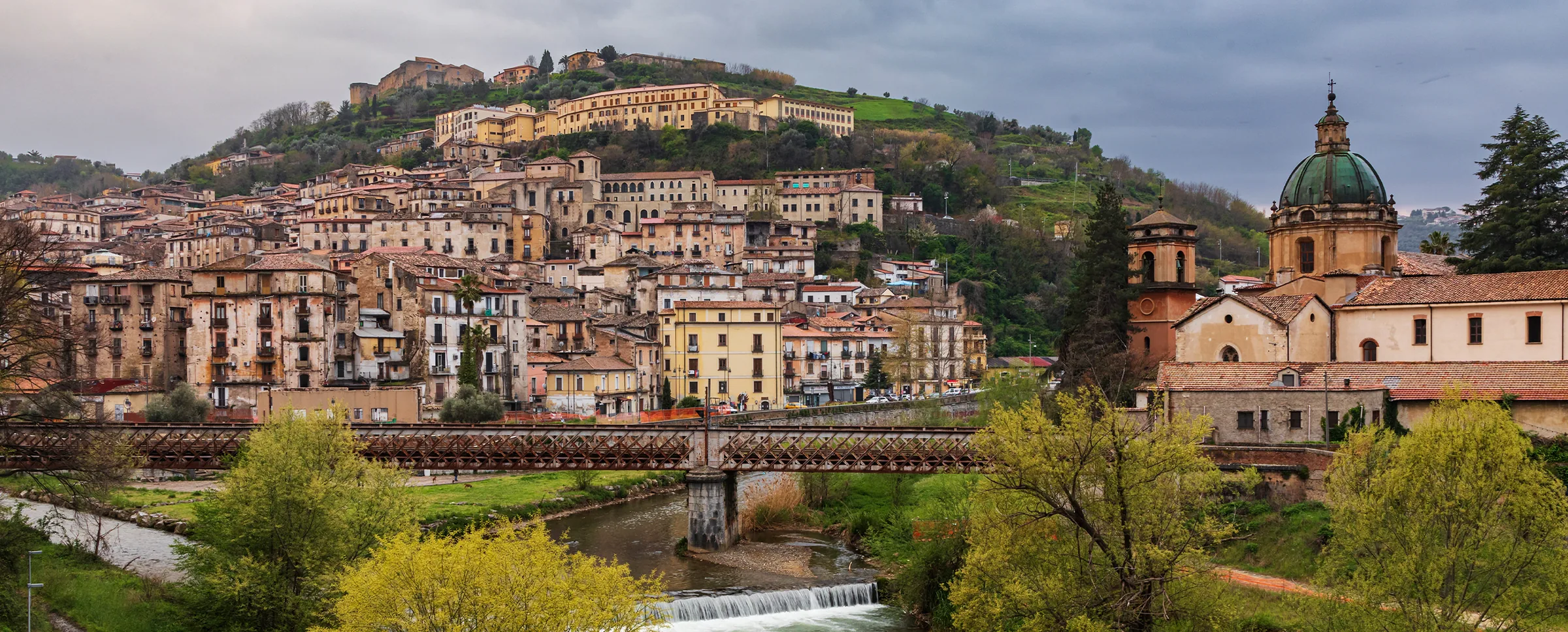 Il centro storico di Cosenza sul colle, con il Castello in cima, un ponte di ferro sul fiume e la cupola di una chiesa sulla destra